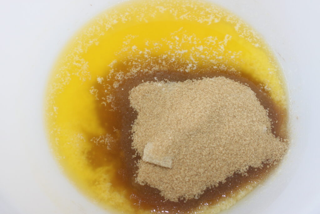 Un bol blanc contenant du beurre fondu, un tas de cassonade et un petit morceau de beurre non fondu ; le début parfait pour un délicieux gâteau aux notes de mégamande.