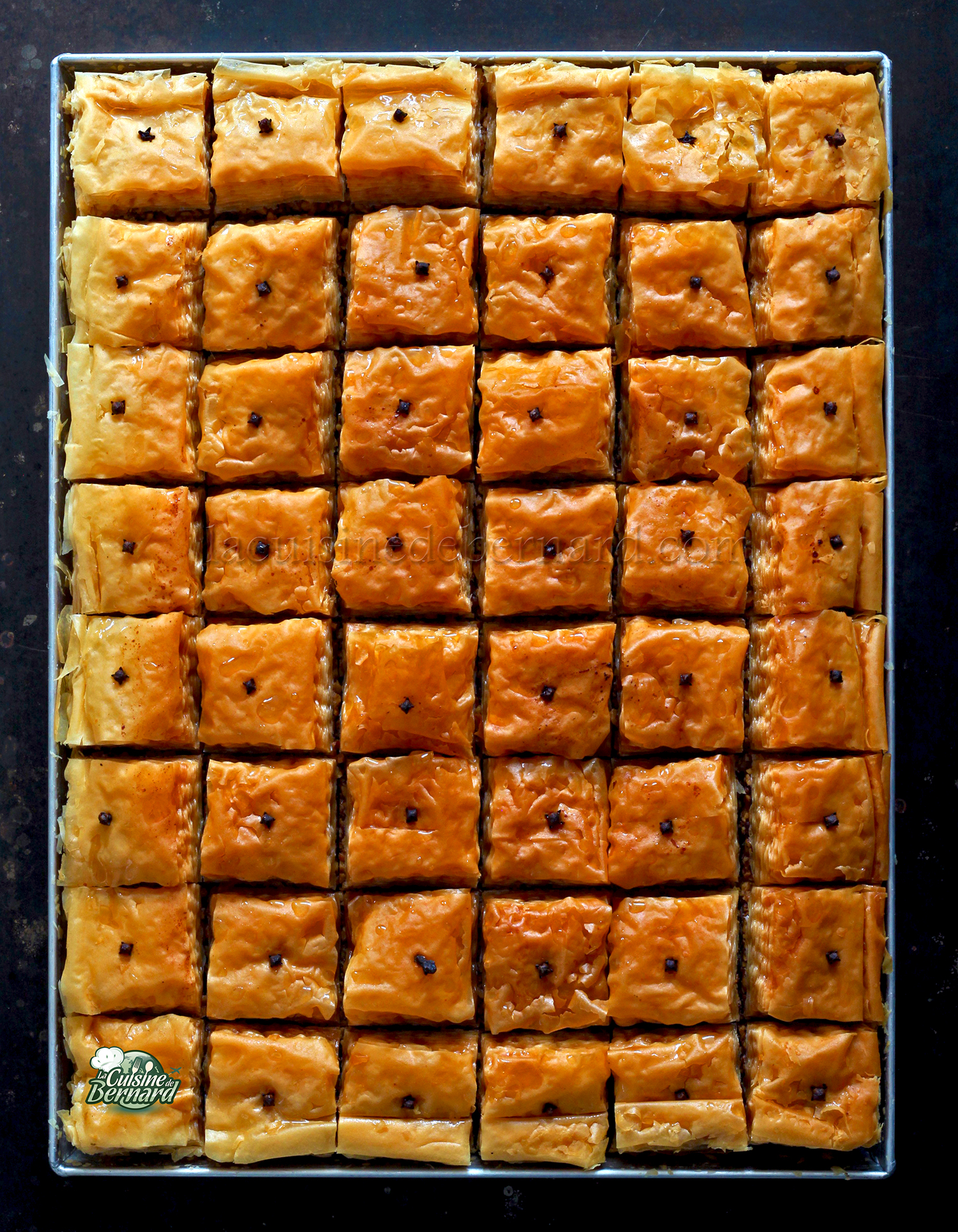 Un plateau de 54 morceaux de baklava brun doré, riches en grecques et en noix, soigneusement disposés en grille et surmontés d'un petit morceau de clou de girofle sur chaque morceau.