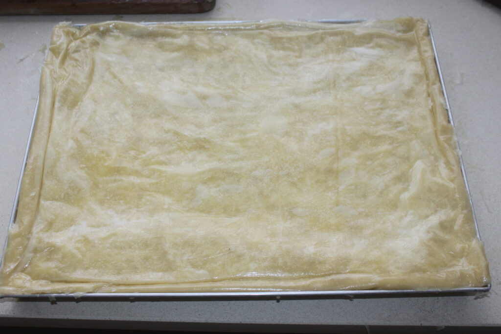 Une plaque à pâtisserie rectangulaire avec une pâte filo crue en couches étalée uniformément sur la surface, prête à être cuite dans un délicieux baklava.