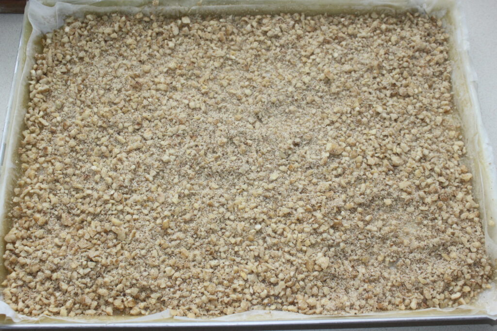 Une plaque à pâtisserie remplie d'une couche de noix concassées, rappelant la base parfaite pour un délicieux Baklava, prêt à être cuit.