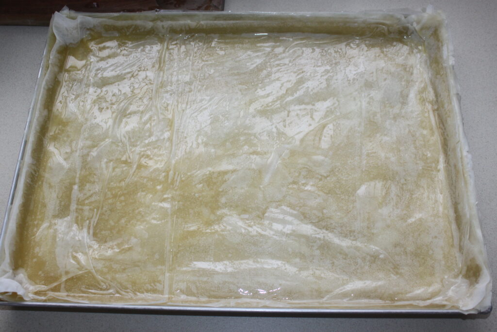 Une plaque à pâtisserie rectangulaire recouverte d'une pâte finement roulée, arrosée d'huile ou de beurre et saupoudrée de noix hachées, prête à cuire un délicieux baklava.
