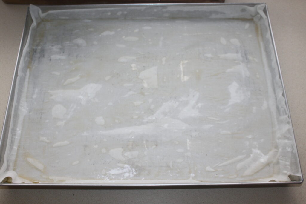 Une plaque à pâtisserie recouverte de papier sulfurisé, graissée de beurre ou d'huile, prête à recevoir un délicieux lot de baklava.