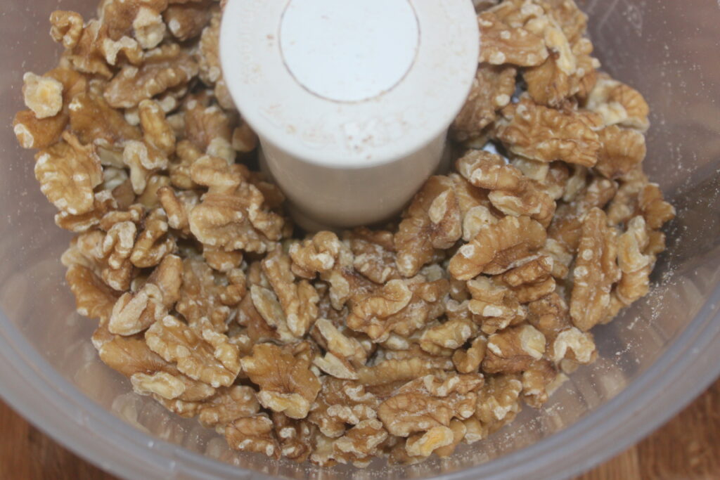 Vue rapprochée des moitiés de noix dans un bol de robot culinaire, prêtes à être hachées ou moulues pour de délicieuses recettes de baklava.
