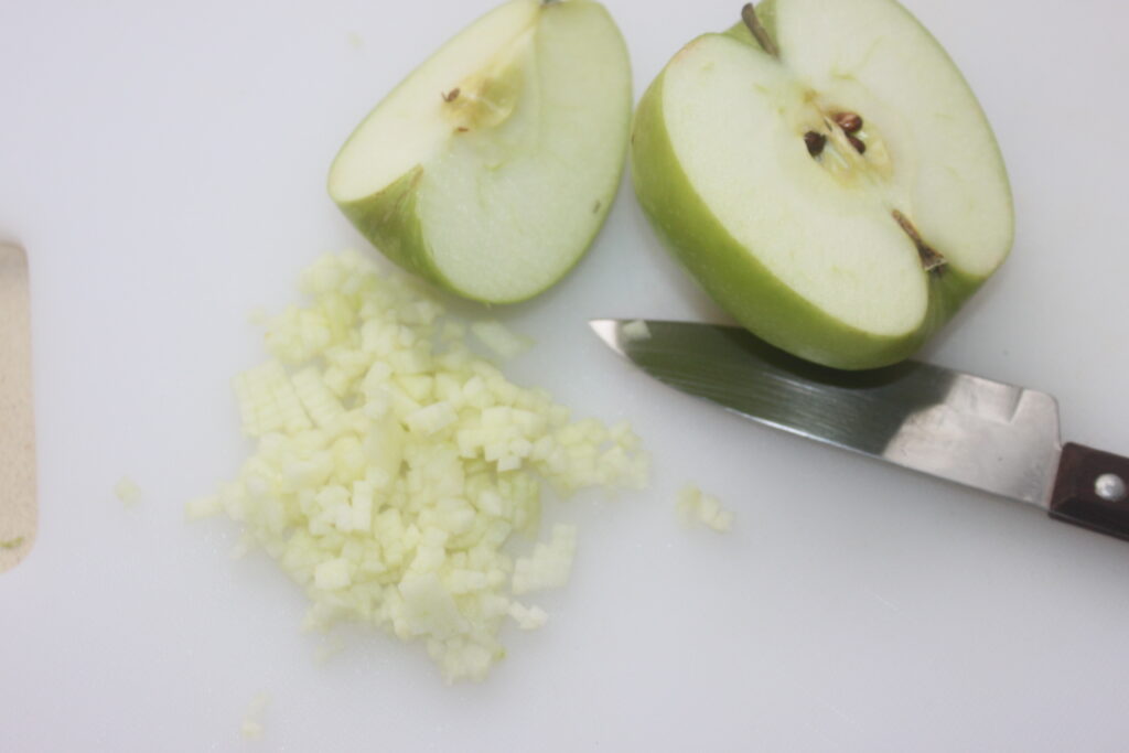 Une pomme coupée en deux avec un couteau d'office à côté, ainsi que des morceaux de pomme finement coupés sur une planche à découper blanche, un peu comme préparer les ingrédients d'un plat de ceviche.
