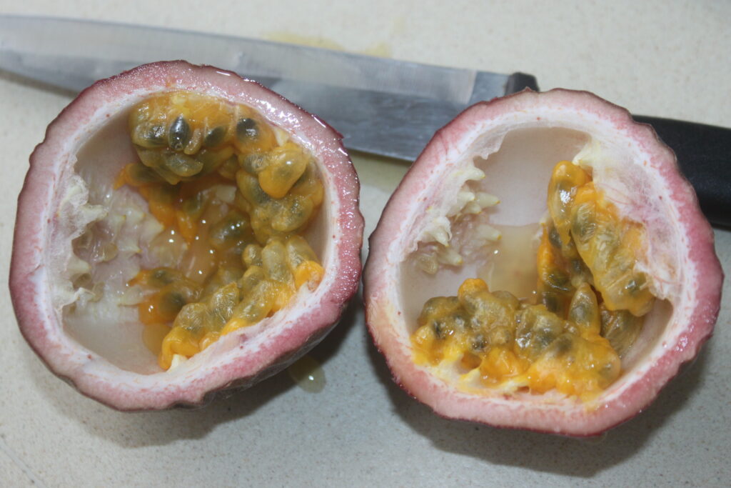 Un fruit de la passion coupé en deux avec les graines et la pulpe exposées se trouve sur une surface de couleur claire à côté d'un grand couteau de cuisine, prêt pour votre prochaine création de ceviche.