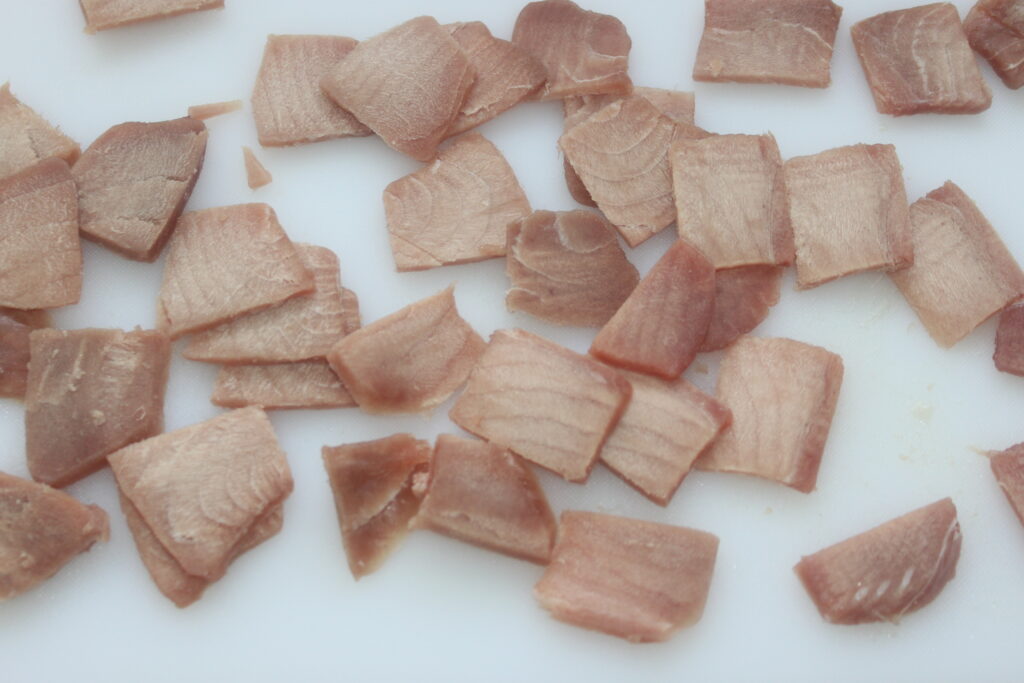 De petits morceaux de thon cru, souvent appelé thon, reposent délicatement sur une planche à découper blanche, prêts à être transformés en un ceviche rafraîchissant.