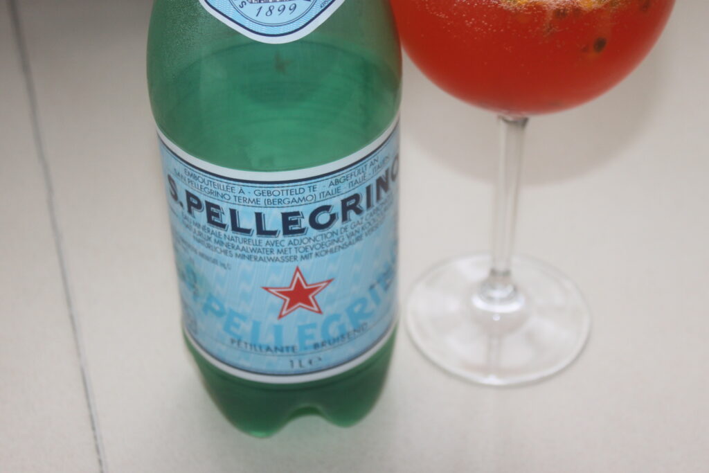 Une bouteille d'eau minérale naturelle gazeuse San Pellegrino côtoie un verre de spritz rouge, parfait pour un moment rafraîchissant au bord de la plage.