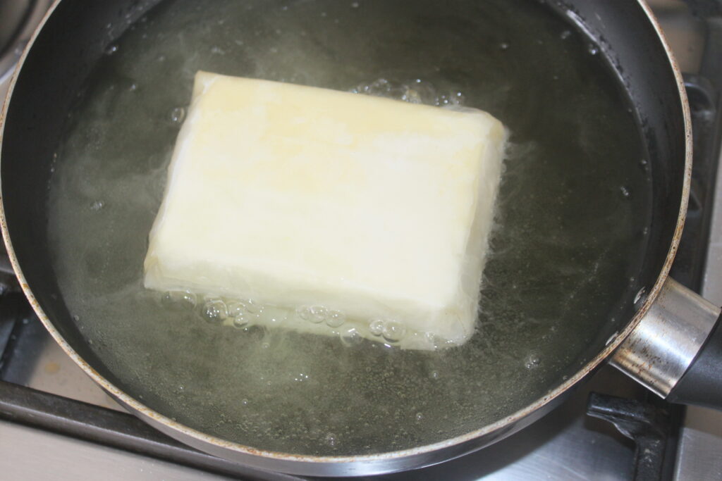 Un bloc de beurre fondant dans une poêle remplie d'eau chaude, créant une base riche parfaite pour arroser une Feta croustillante croustillante.