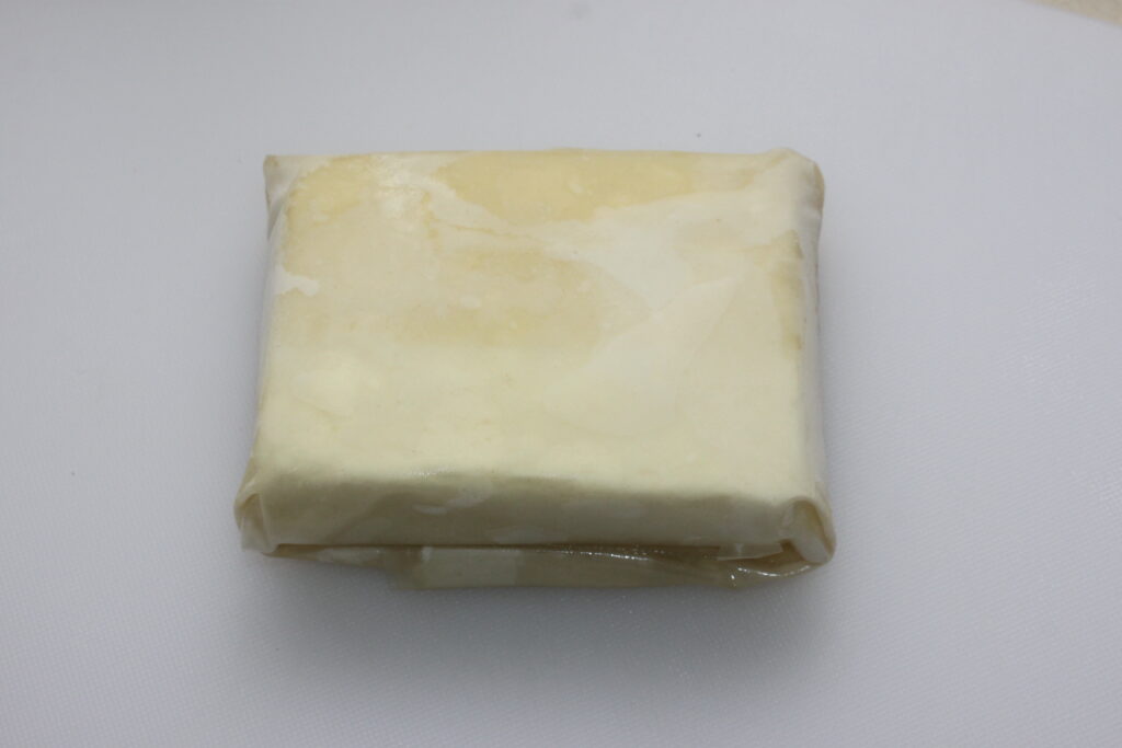 Un bloc de beurre enveloppé dans du papier sulfurisé, posé sur une surface blanche, évoque une simplicité semblable au miel arrosé d'une pâtisserie délicate.