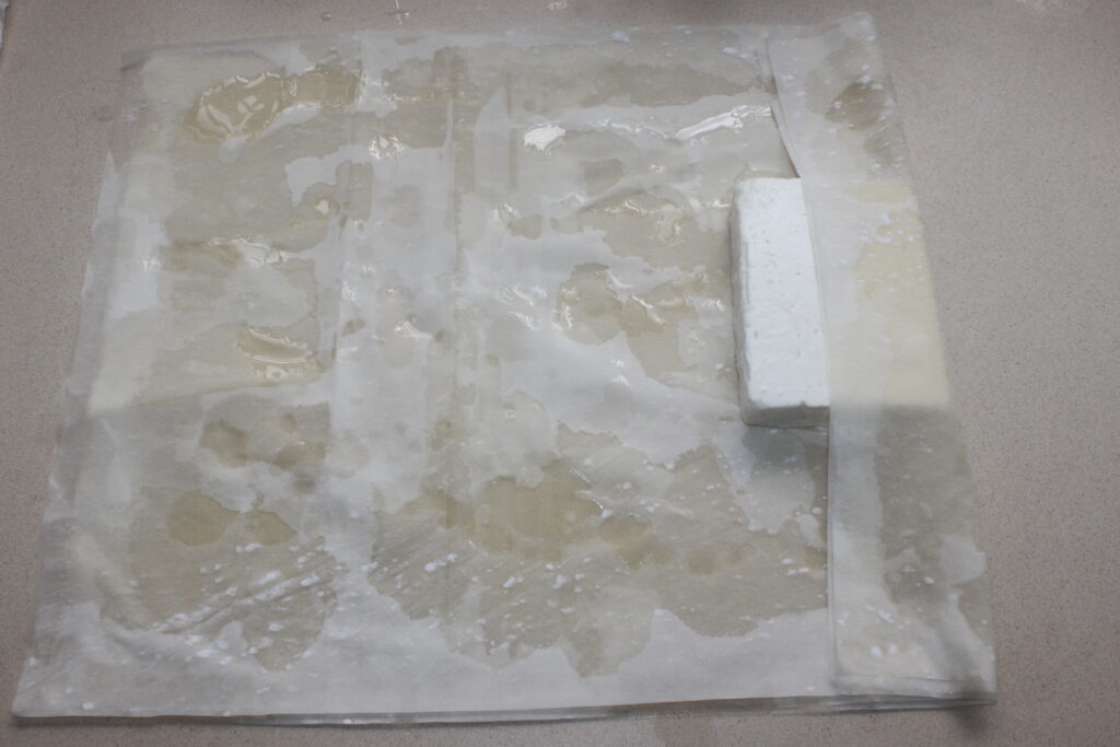 Un bloc de tofu est placé sur des couches de serviettes en papier humides, qui absorbent l'humidité comme du miel un jour d'été.