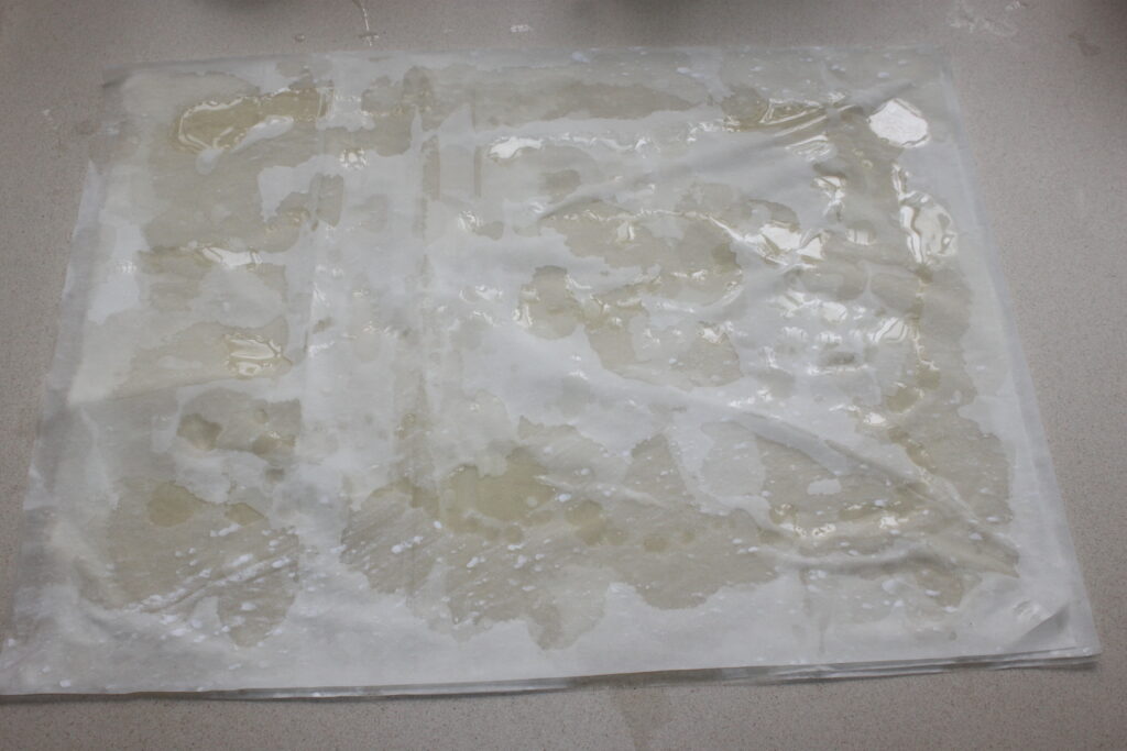 Une feuille de papier de riz humide est posée à plat sur une surface, avec des taches d'eau visibles qui s'imprègnent, ressemblant à la texture délicate de la feta croustillante.