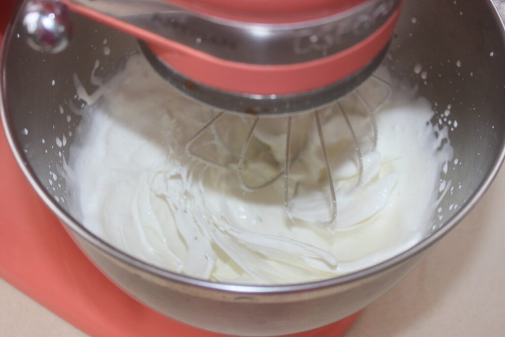 Un batteur sur socle rouge fouette le mascarpone chantilly dans un bol en acier inoxydable pour de délicieuses tartelettes fraise.