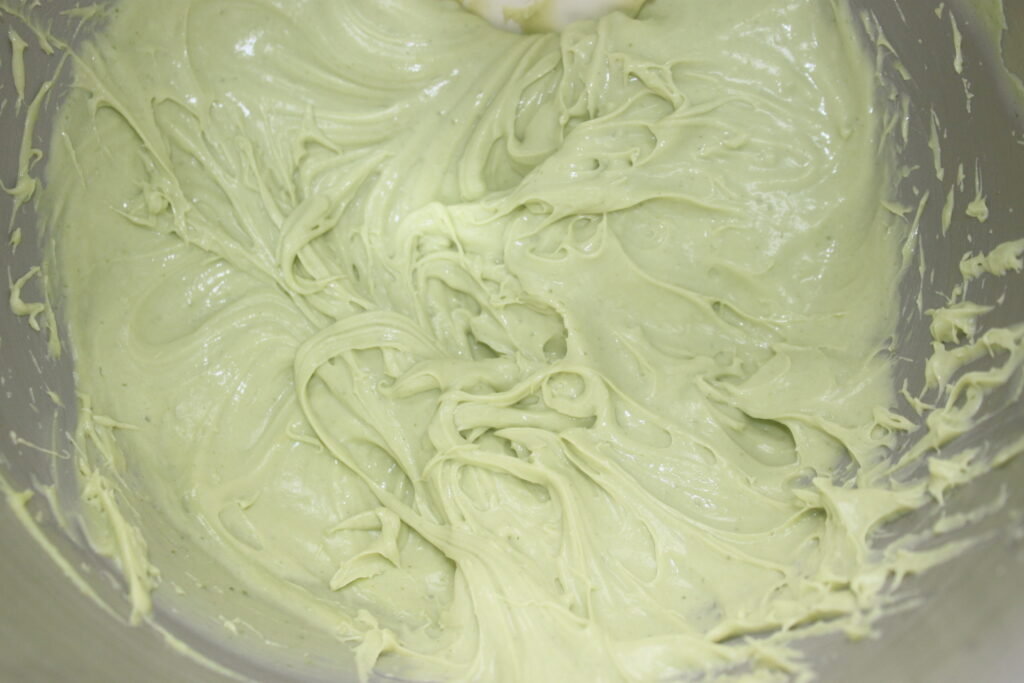 Gros plan d'un bol à mélanger rempli de pâte à base de crème basilic vert pâle, montrant une texture lisse et crémeuse avec des tourbillons.