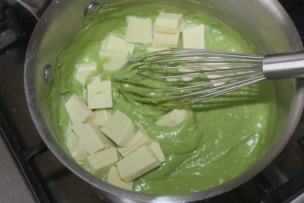 Un fouet en remuant les cubes de chocolat blanc dans un mélange vert épais de crème basilic chocolat blanc dans une casserole sur une cuisinière.