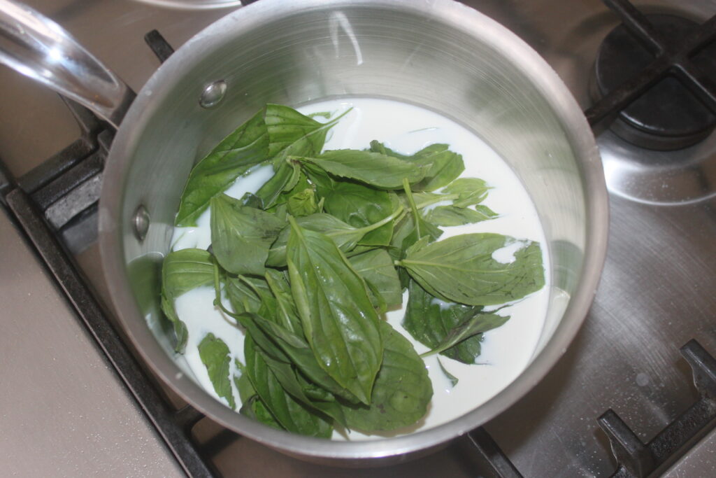 Une marmite en métal sur une cuisinière contient des feuilles de basilic vert frais et une petite quantité de lait, créant la base parfaite pour une exquise sauce au chocolat blanc au basilic.