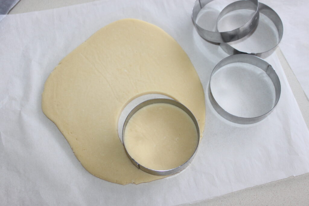 Une tranche de pâte est étalée sur du papier sulfurisé, avec des emporte pièces circulaires à côté. Un emporte pièce permet de découper dans la pâte une forme circulaire, prête à être transformée en délicieuses tartelettes fraîches garnies de chantilly mascarpone.