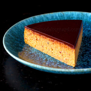Une tranche de gâteau fondant à l'orange garnie de chocolat repose sur une assiette en céramique bleue sur fond sombre.