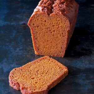 Une miche de pain brun avec une tranche coupée et placée devant elle sur une surface sombre.