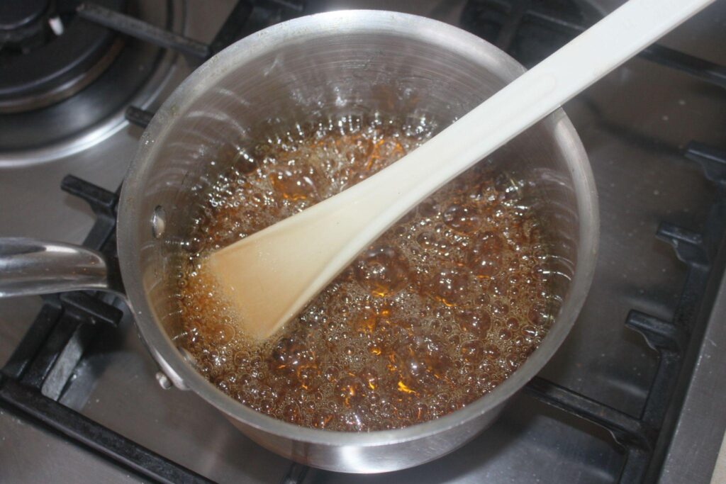 Une casserole avec du sucre caramélisé bouillonnant sur une cuisinière, remué avec une spatule blanche.