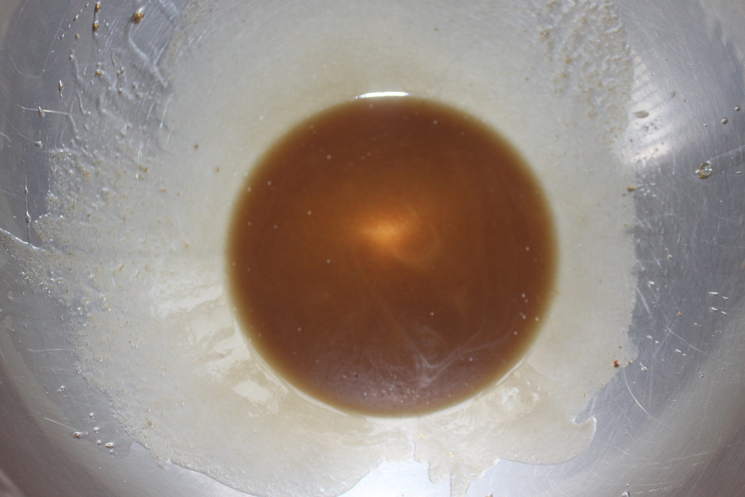 Une petite quantité de liquide brun se trouve au centre d'un bol en acier inoxydable, avec quelques résidus visibles sur les côtés une scène rappelant une auto Brouillon en cours.