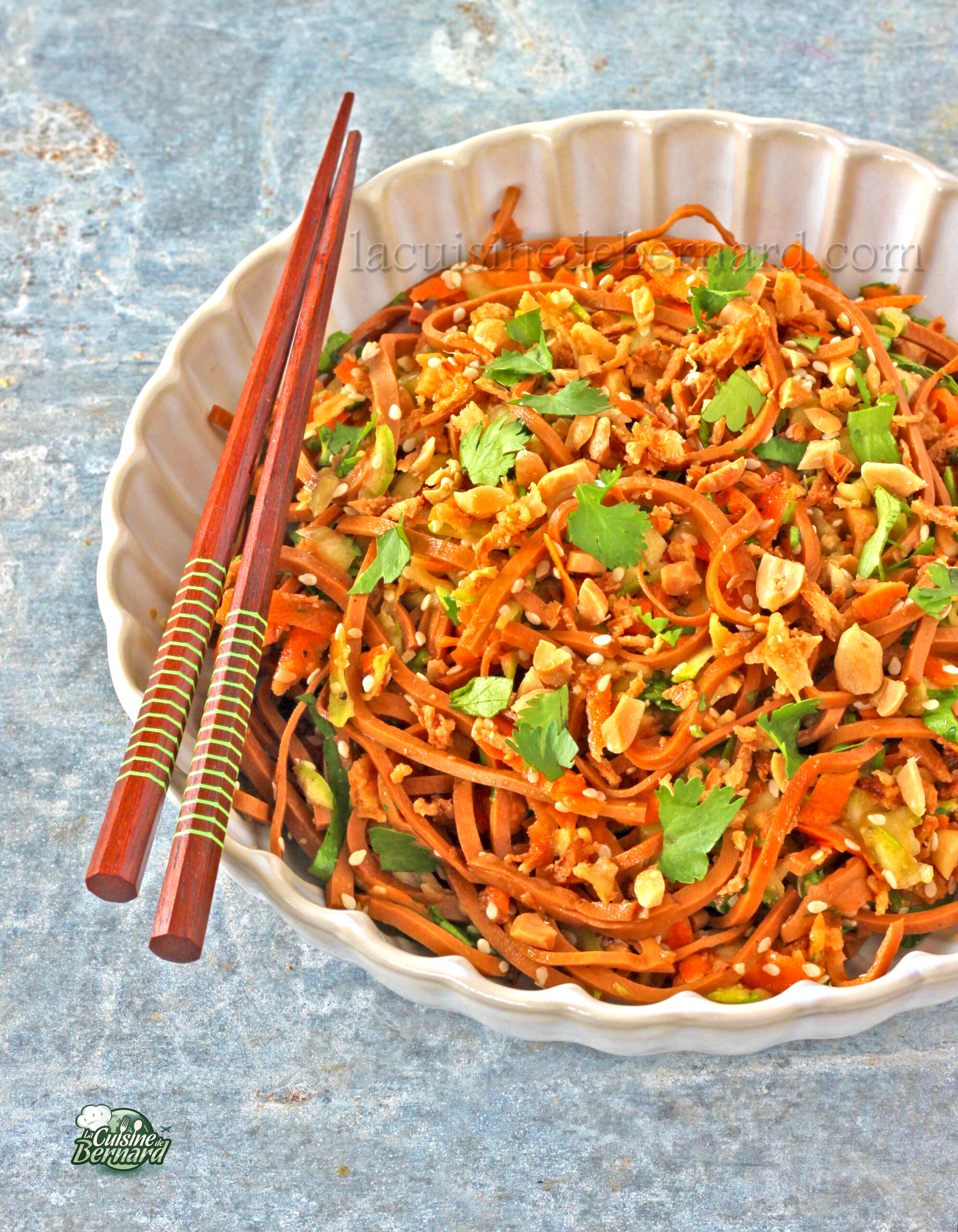 Un bol de salade de tofu garni de cacahuètes hachées et de coriandre, accompagné d'une paire de baguettes en bois à côté – une recette santé idéale pour les amateurs de salade de nouilles.