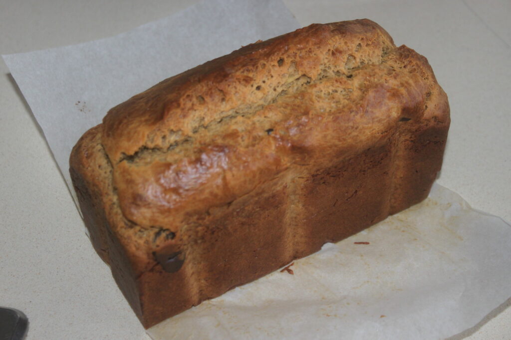 Une miche de pain maison à la croûte dorée et au dessus fendu est posée sur du papier sulfurisé, remplie d'un irrésistible arôme de banane et de cacahuète.
