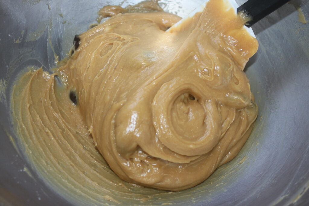 Pâte à biscuits épaisse mélangée dans un bol en métal à l'aide d'une spatule, parfaite pour créer un délicieux gâteau banane ou même un indulgent gâteau cacahuète.
