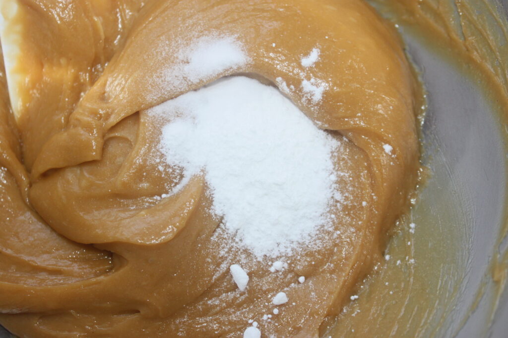 Pâte épaisse de couleur marron clair pour gâteau cacahuète ou gâteau banane, recouverte d'un monticule de levure chimique blanche dans un saladier.