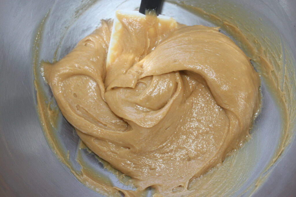 Un saladier contenant de la pâte à biscuits crémeuse et marron clair pour le gâteau cacahuète est remué à l'aide d'une spatule en caoutchouc.