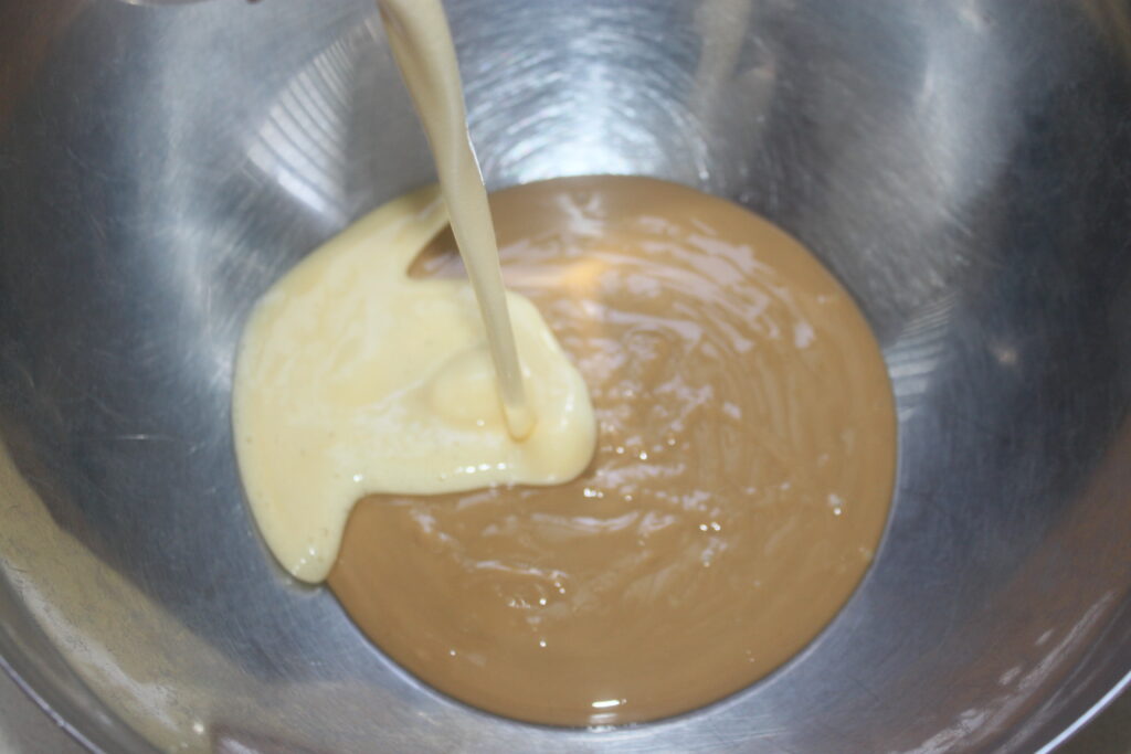 Un liquide épais de banane pâle est versé dans un bol en acier inoxydable contenant un mélange de cacahuète brun clair.