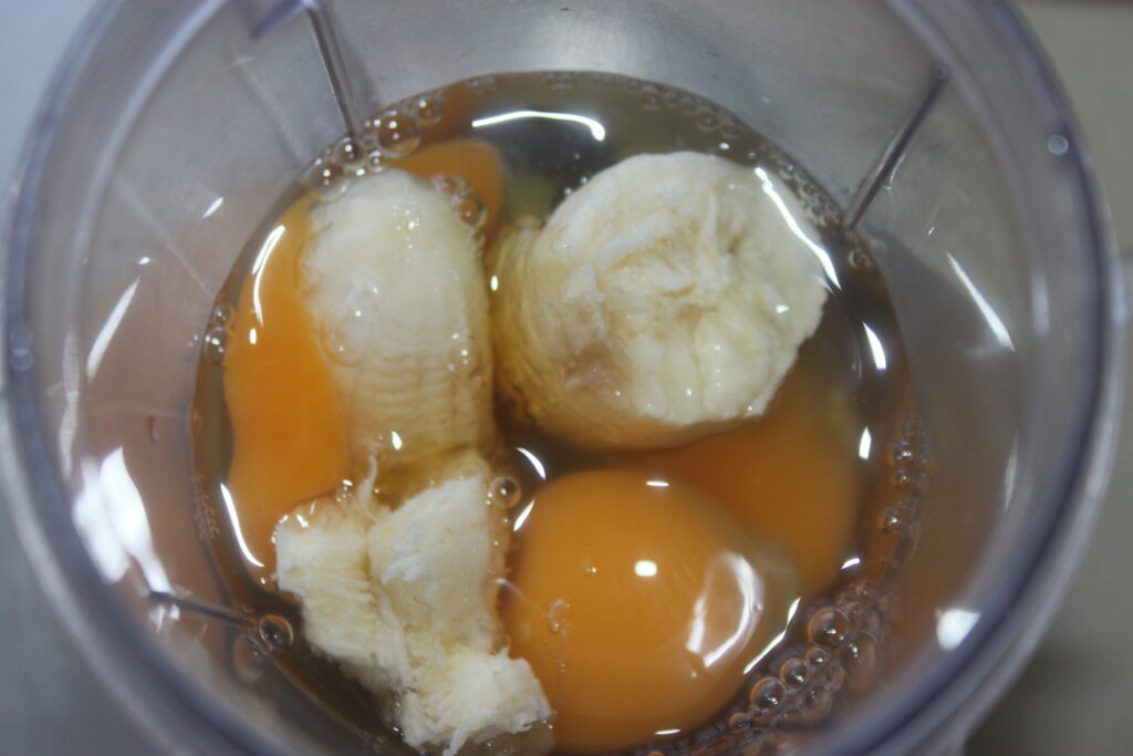 Deux œufs crus et des morceaux de banane dans le gobelet d'un mixeur, prêts à être mélangés parfait pour créer un délicieux gâteau banane.